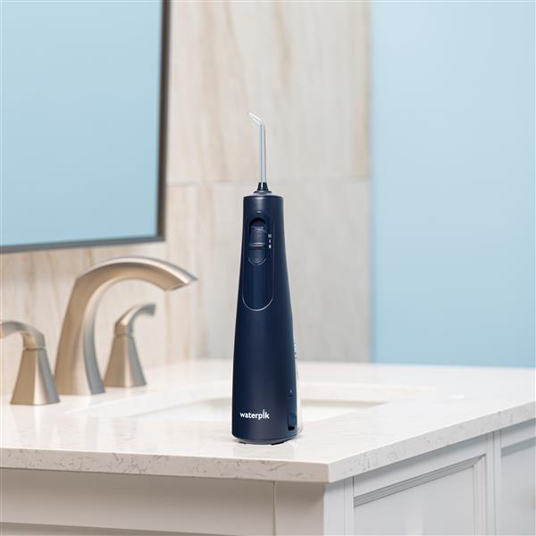 Blue Cordless 1000 handheld water flosser on a bathroom sink.