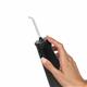 Black Cordless Plus 5000 handheld water flosser handle and EASYSPIN 360° rotating tip, shown held in a hand for scale.
