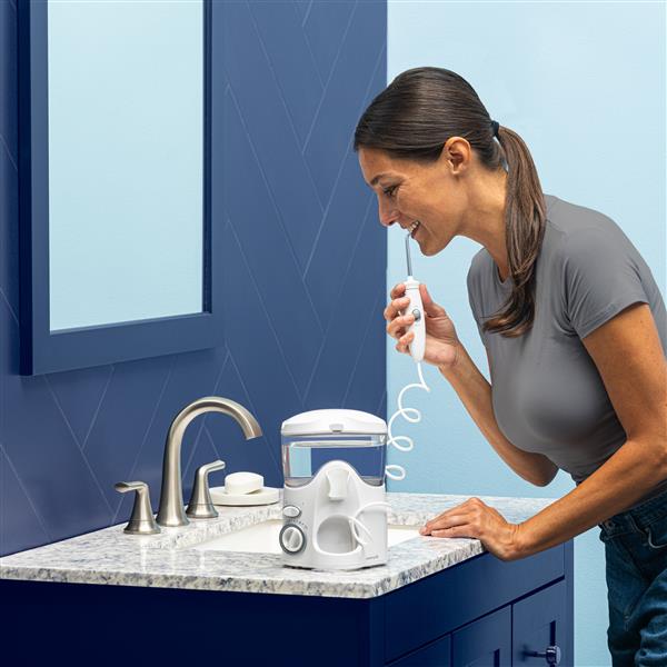 White Ultra countertop water flosser in use, with person leaning over the bathroom sink.