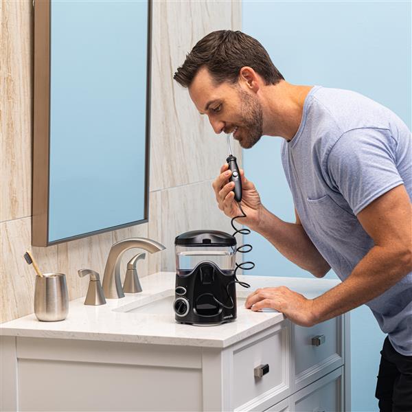 Black Ultra countertop water flosser in use, with person leaning over the bathroom sink.