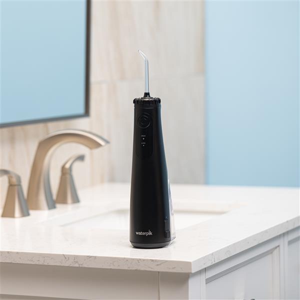 Hydropulseur portatif sans fil Plus 5000 noir sur un lavabo de salle de bain.