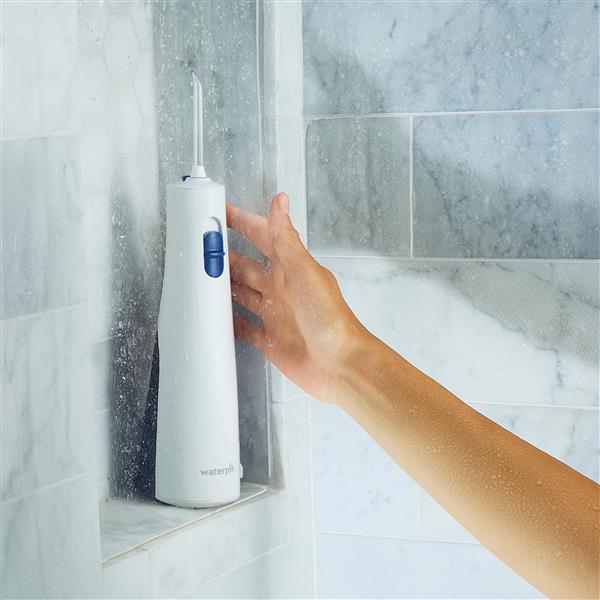 Hydropulseur sans fil 1000 blanc sur un rebord de douche, une main tendue vers l’appareil.