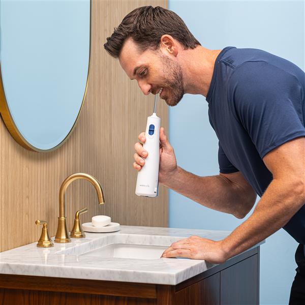 Hydropulseur portatif sans fil 1000 blanc en cours d’utilisation, une personne penchée au-dessus du lavabo de la salle de bain.