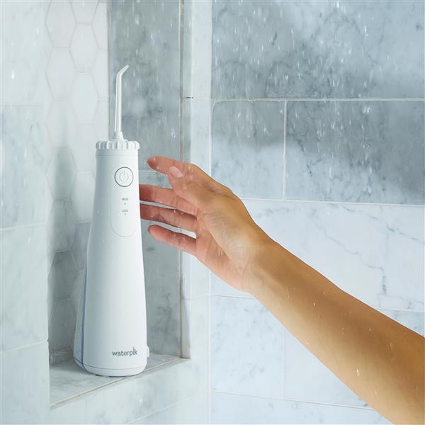 Hydropulseur sans fil Plus 5000 blanc sur un rebord de douche, une main tendue vers l’appareil.