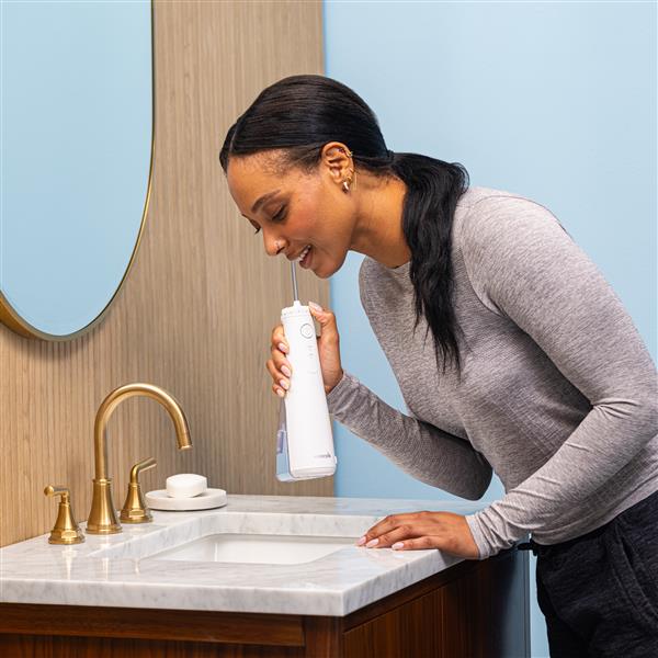 Hydropulseur portatif sans fil Plus 5000 blanc en cours d’utilisation, une personne penchée au-dessus du lavabo de la salle de bain.