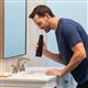 Hydropulseur portatif sans fil Plus 5000 noir en cours d’utilisation, une personne penchée au-dessus du lavabo de la salle de bain.
