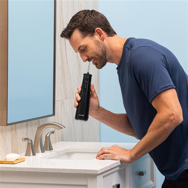 Hydropulseur portatif sans fil Plus 5000 noir en cours d’utilisation, une personne penchée au-dessus du lavabo de la salle de bain.